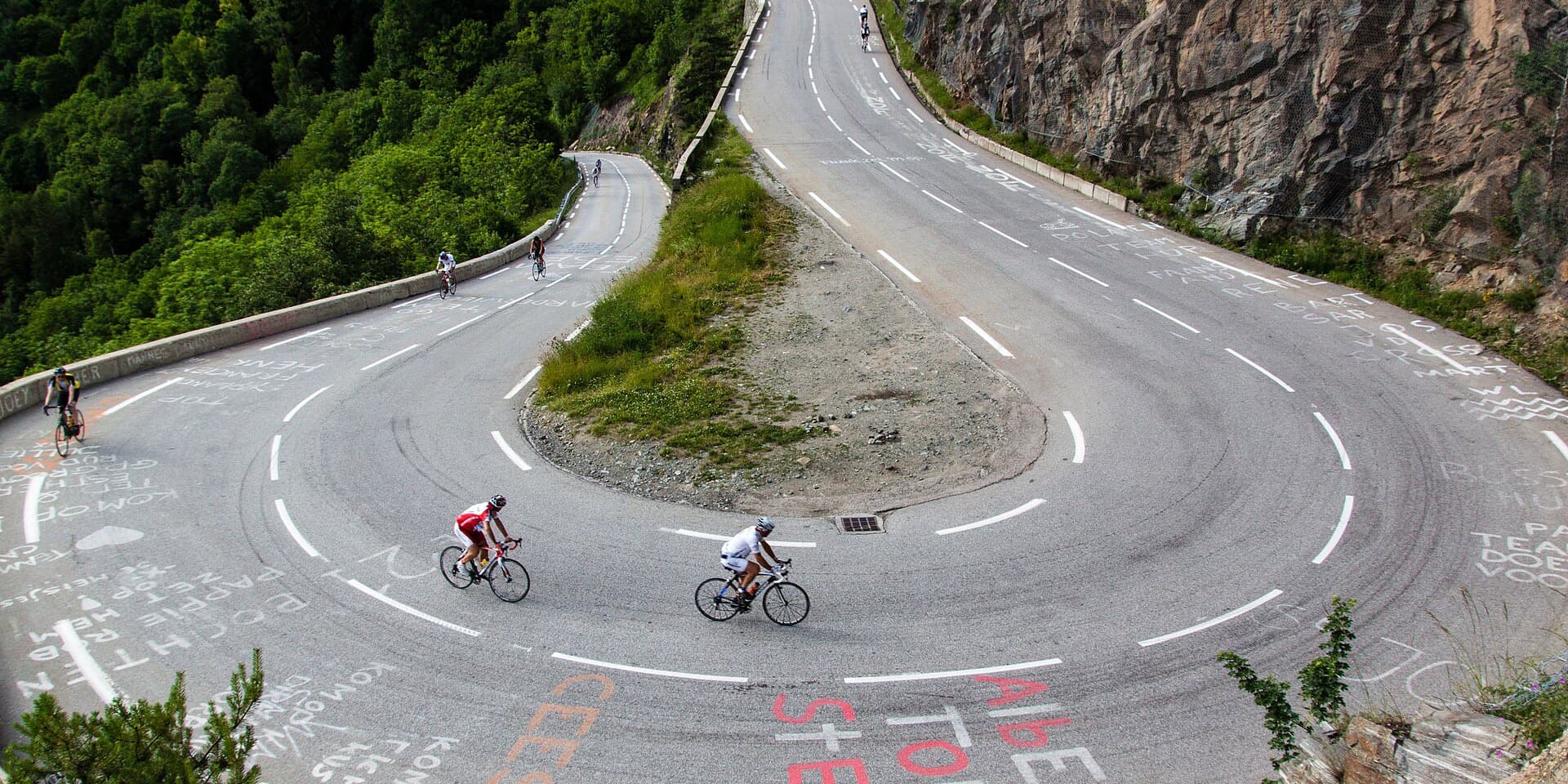 Wielrenners in een haarspeldbocht van Alpe d'Huez, met namen van fans op het asfalt