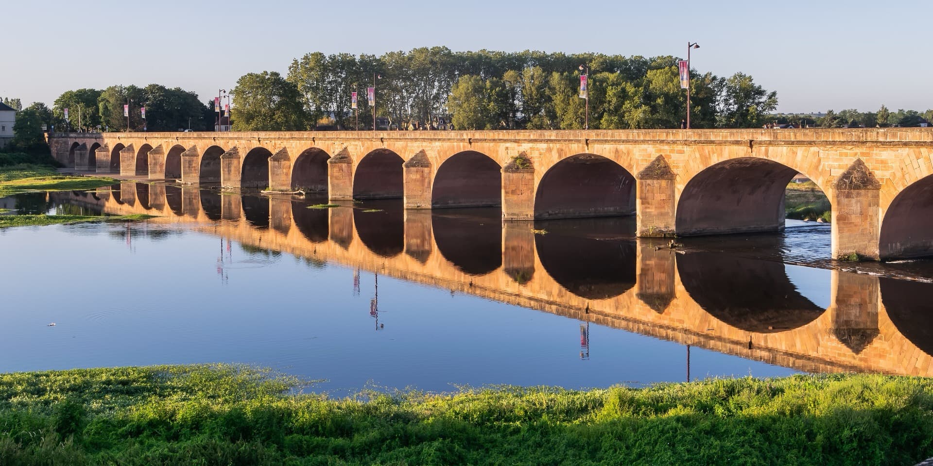 The stone arches of the Pont de Loire in Nevers, mirrored in the river